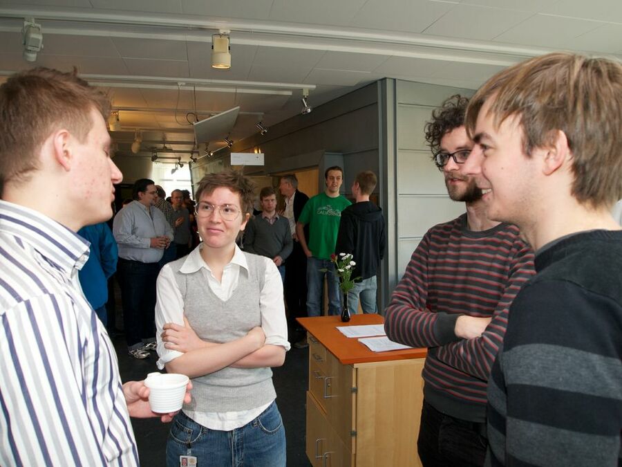 Four participants having a discussion at a break with other participants in the background.